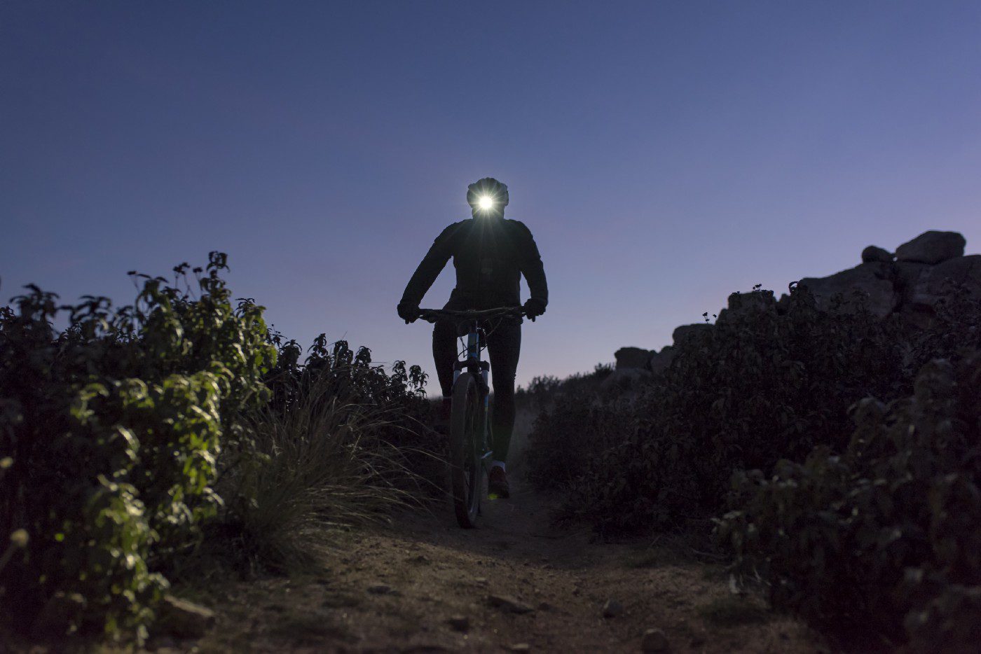 Un cycliste avance dans la nuit guidé par une lampe frontale